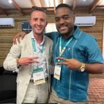 Two men, delegates at a tourism conference, pose with arms around each other. Dustin Rennie and Jalen AVILA with Beltraide.